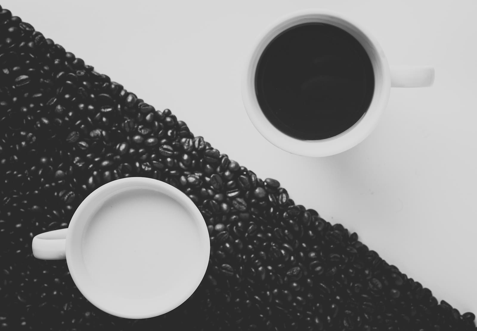 Two coffee mugs, black and white, set against a black and white background in the manner of a yin yan symbol, indicating lifestyle D/s is about symbiosis and balance