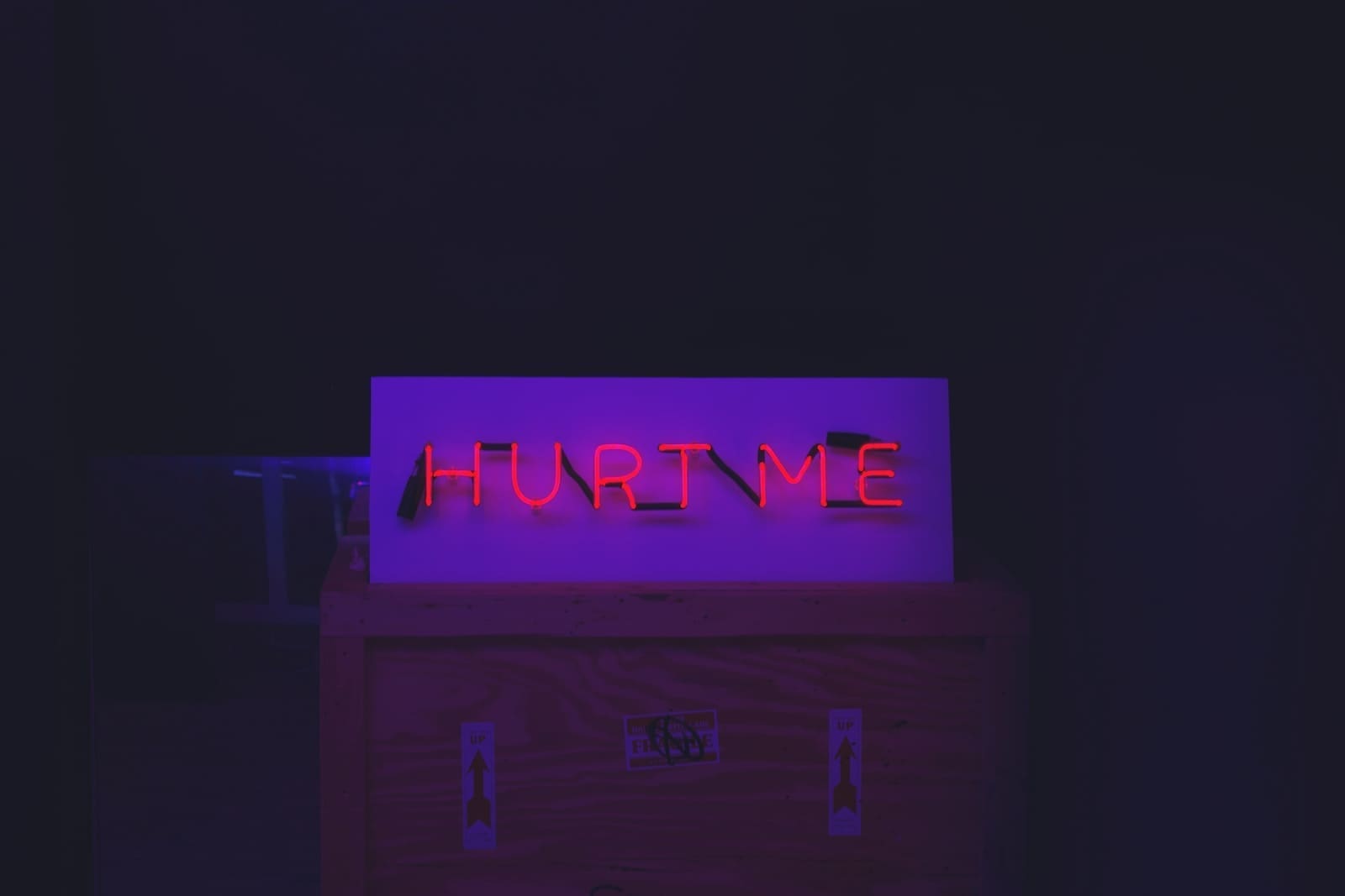 Red neon "Hurt Me" sign on top of a crate with arrow stickers